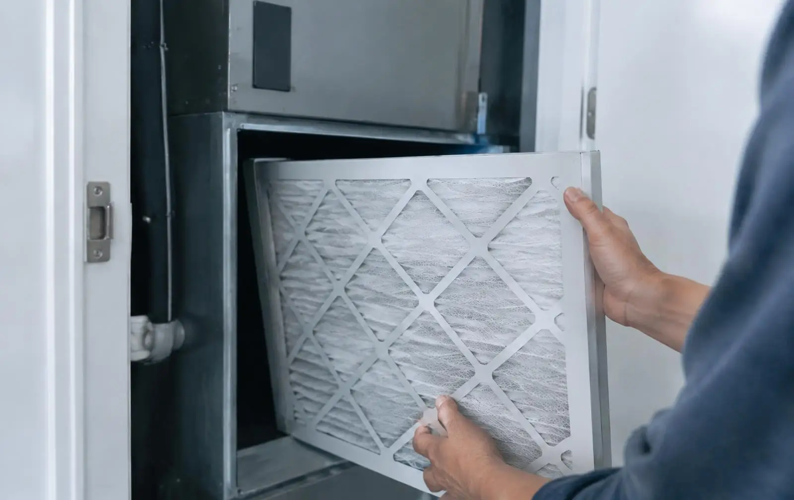 Hands sliding a clean pleated air filter into an indoor air handler